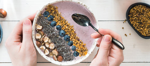 Eating healthy breakfast bowl. Buckwheat smoothie porrige, fresh berries, seeds and nuts, bee pollen in white ceramic bowl in woman hands on table. Clean eating, dieting,detox, vegetarian food concept