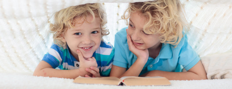 Child reading book in bed under knitted blanket