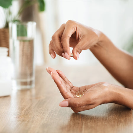 capsules in womans hands with glass of water