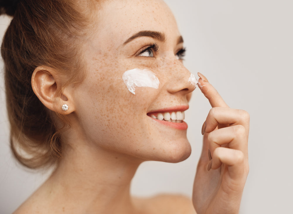 smiling girl applying moisturiser to nose and cheek