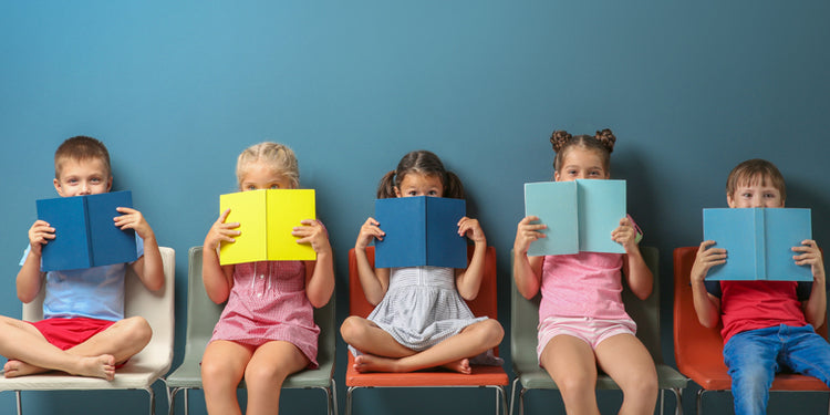 School age children sitting in a row hiding their faces behind books