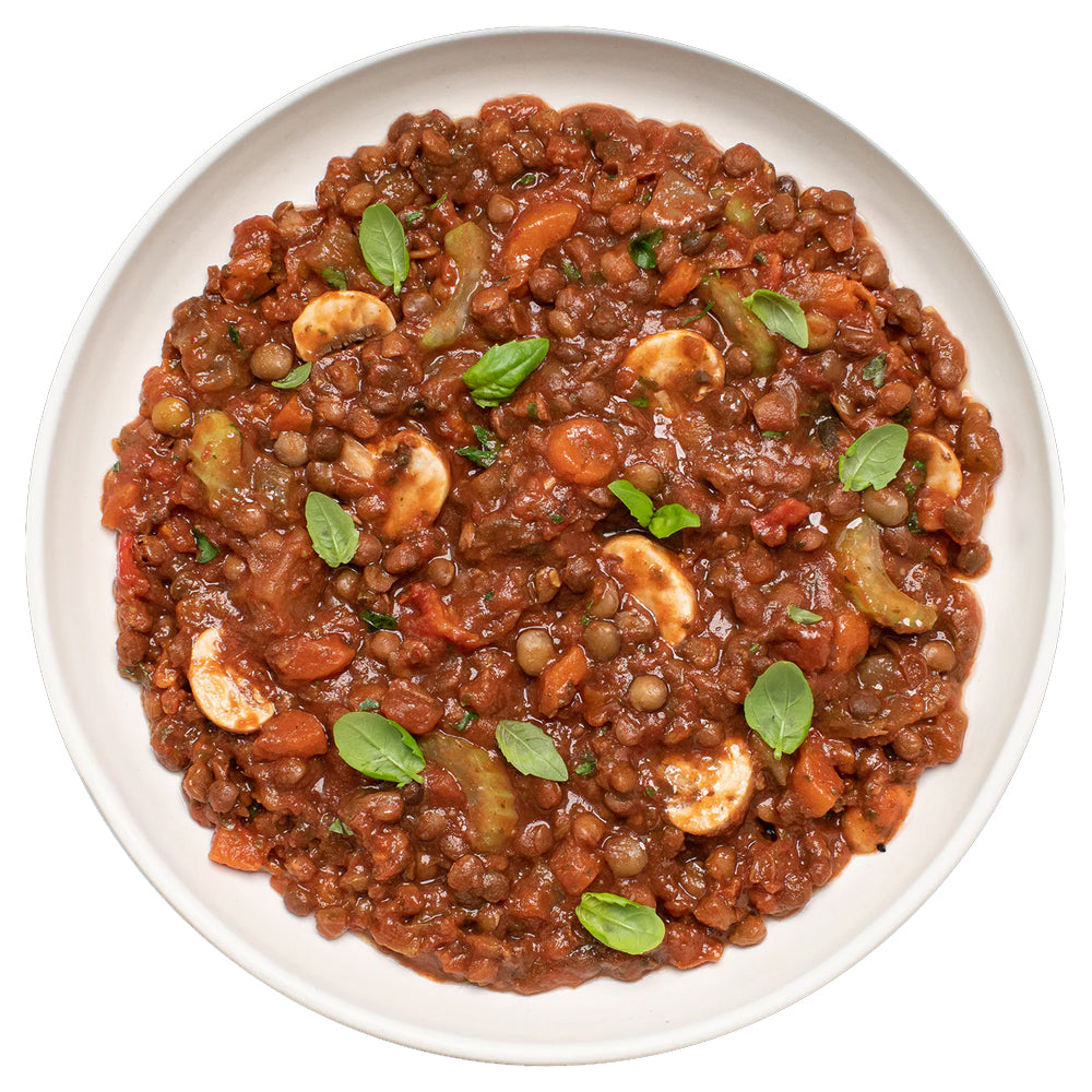 Plated dish of lentil stew with cashews and herbs on a white background
