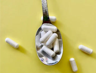 White supplement capsules on spoon on yellow background