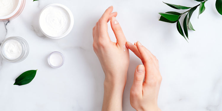 female hands applying cream with jars and leaves in background