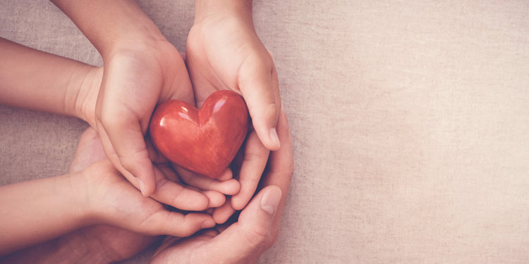 A family cupping hands holding a red heart