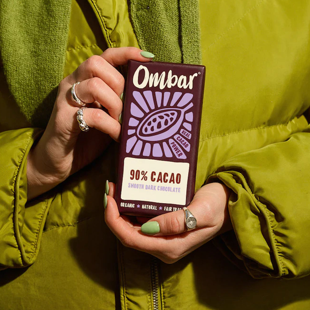 Person holding an Ombar 90% Cacao chocolate bar against a green jacket.