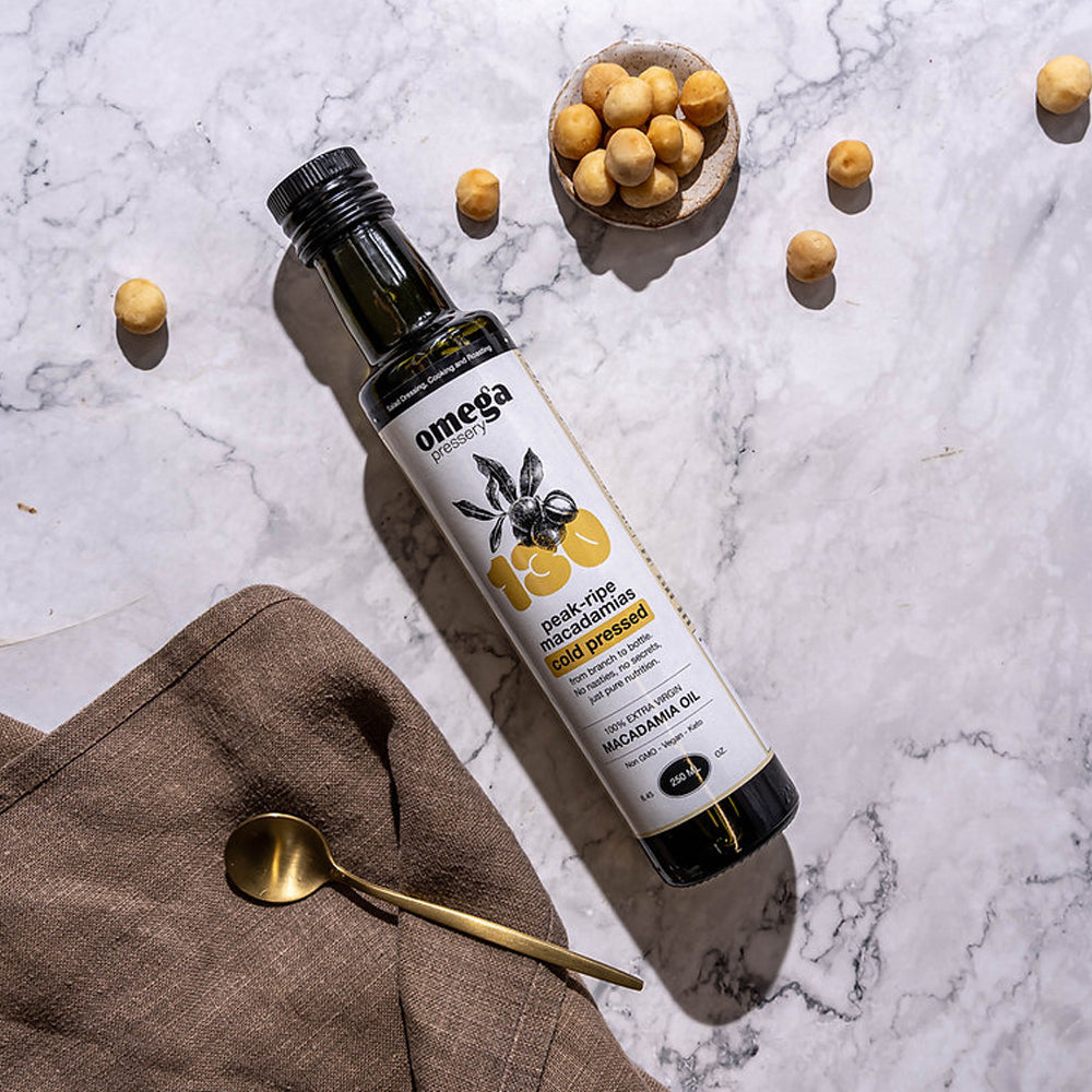 Bottle of Omega Macadamia Oil on a marble surface with macadamias and a spoon.