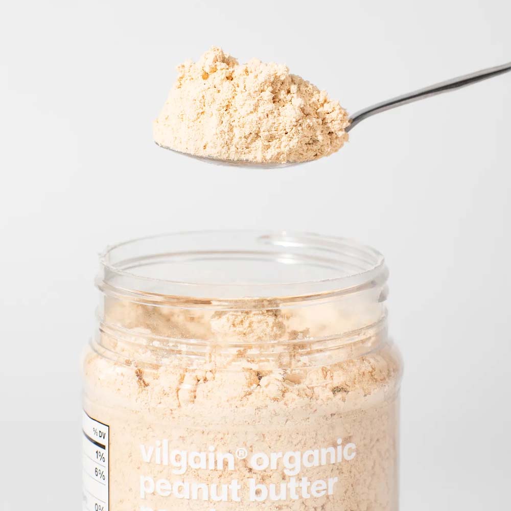 A clear jar of Vilgain Organic Peanut Butter with a spoonful of the beige powder