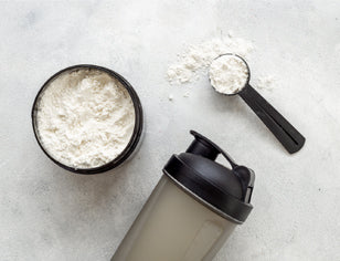 White protein powder in black tub with shaker bottle