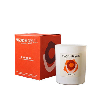 A white glass vessel candle and orange box for the Wizard & Grace "Courage" natural essential oil candle, featuring abstract concentric oval artwork in red, orange, and light pink.