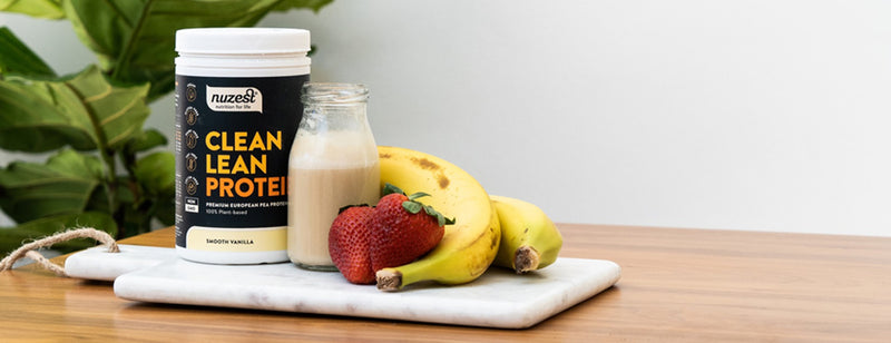 nuzest tub with smoothie, banana and strawberries on wooden board