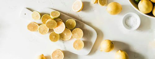 white countertop with chopping board containing lemons beside a small white bowl of salt