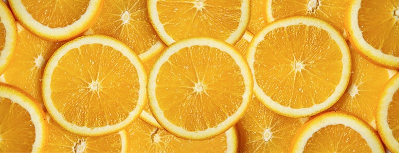Close-up view of multiple overlapping fresh orange slices, showing the bright yellow-orange colour and juicy texture.