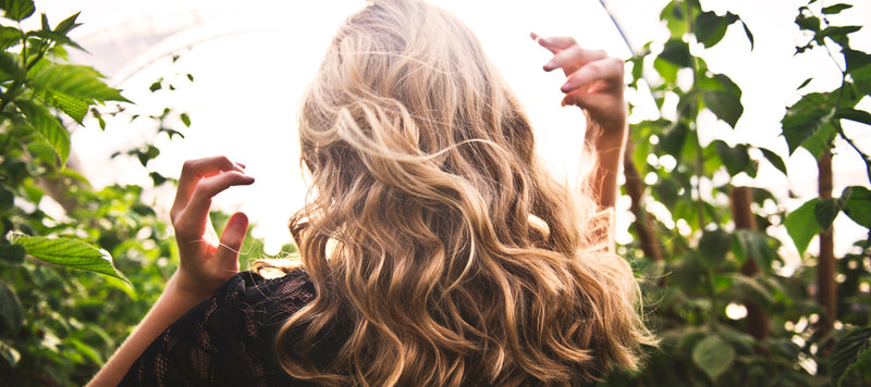 woman with beautiful long blonde curly hair, with plants in the background