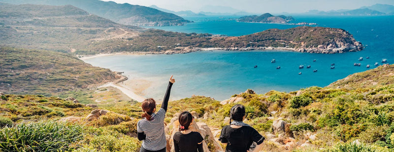 Three women on holiday on top of a hill, looking out at the ocean