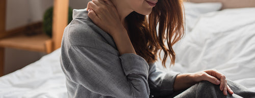 woman who has fibromyalgia sitting on bed holding sore neck