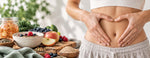Woman forming a heart shape over her stomach beside fibre-rich foods, berries and fermented vegetables, representing gut health and digestive wellbeing.