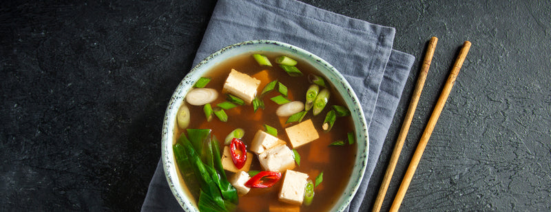 bowl of Japanese style miso and vegetable soup on a napkin beside chopsticks 