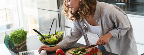 woman preparing a healthy meal while checking recipe on the laptop