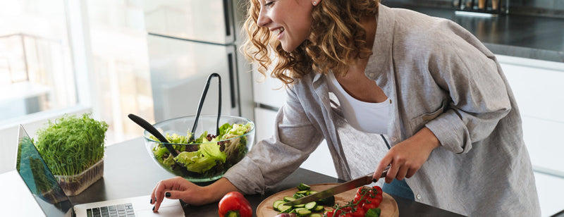 woman preparing a healthy meal while checking recipe on the laptop