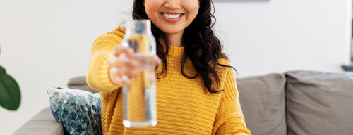 smiling woman holding out a bottle of water, staying hydrated