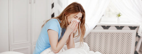 woman with sinus and nasal congestion blowing nose in bed