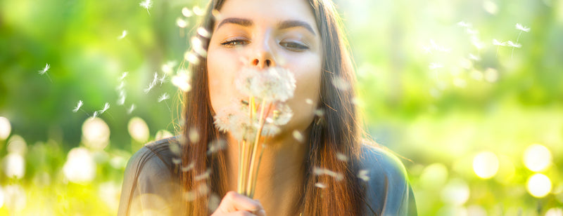 woman blowing dandelion in field trying to survive hay fever season