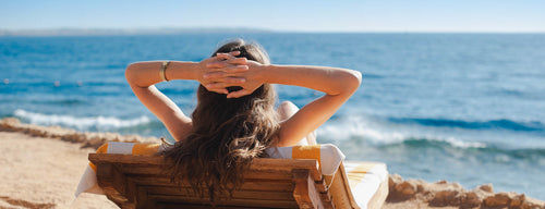 woman sunbathing on sun lounger looking at the sea wearing natural sun protection