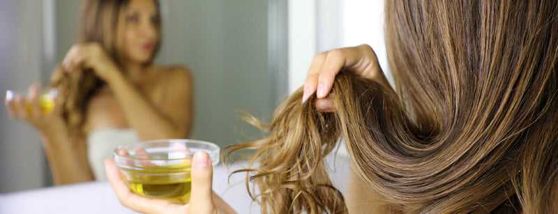 Woman applying natural hair oil in bathroom mirror