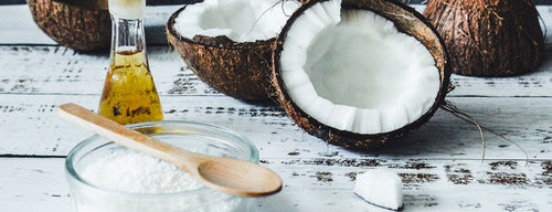 top uses for coconut oil, with wooden spoon, open coconut and glass of oil