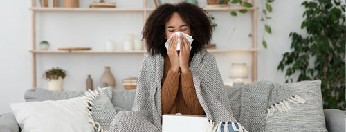 woman who is sick during winter blowing her nose on the couch 