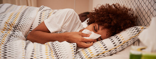 sick woman blowing her nose in bed with a bacterial or viral infection