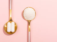 powder and capsule supplements on gold spoons on a pink background