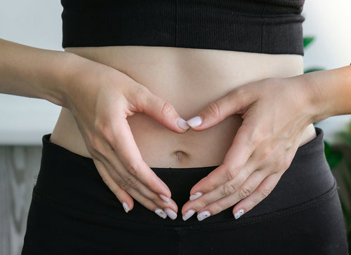 woman in black trousers and top making heart shape with hands over stomach