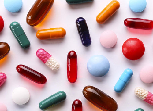 brightly coloured tablets and capsules on pink backgroun