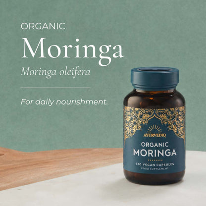 A bottle of Ayurveda Organic Moringa capsules on a light surface. White text on the left reads &