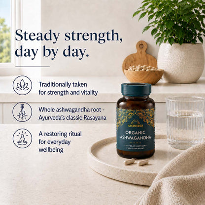 Organic Ashwagandha herbal supplement bottle on a tray with capsules, styled on a windowsill with a glass of water, potted plant, and text describing its benefits.