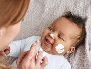 Smiling baby having face cream applied