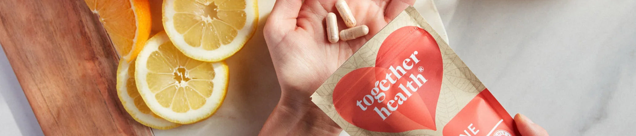 Hand holding a packet labeled 'Together Health' with sliced lemons on a wooden board.