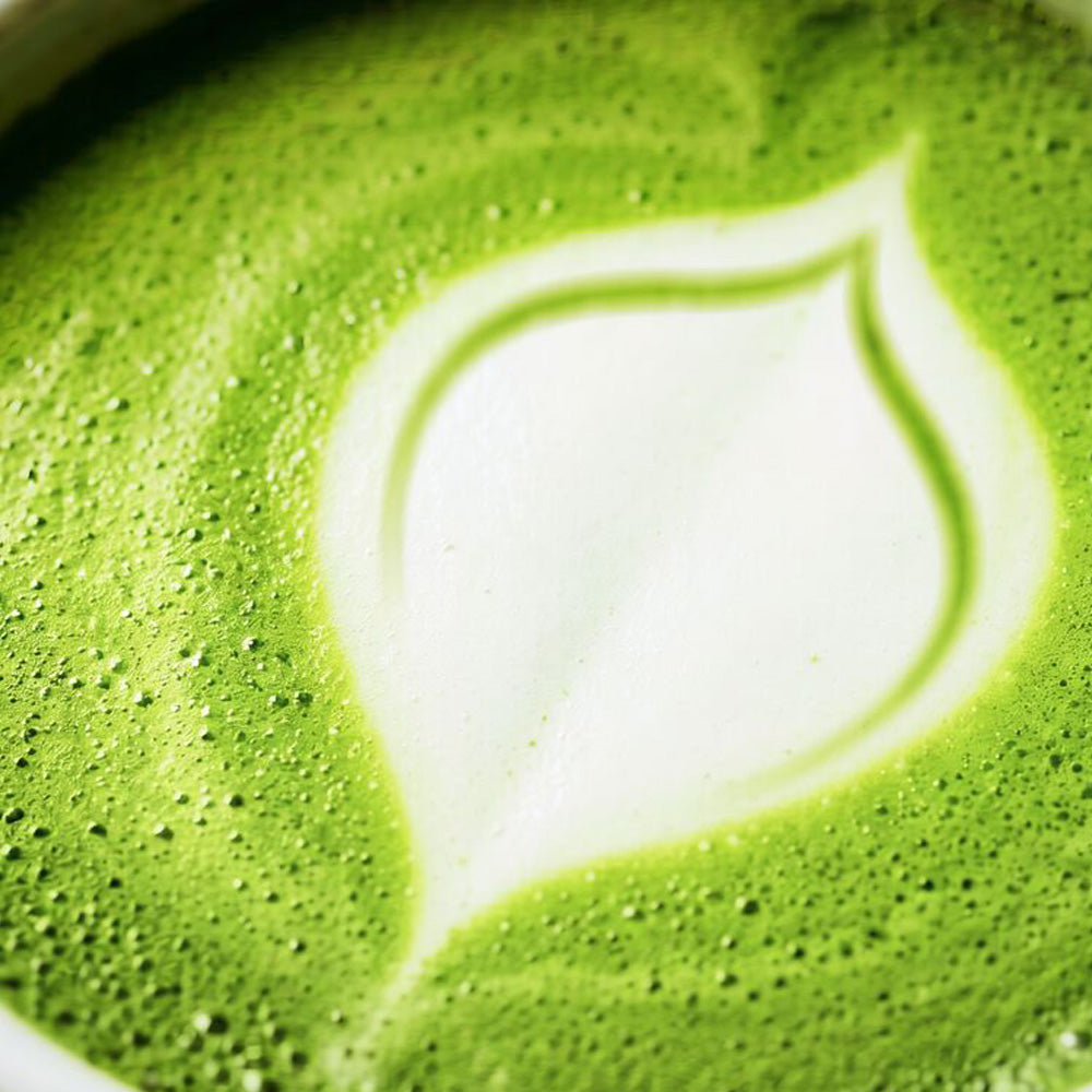 Close-up of a green matcha latte with a white leaf-shaped foam design on the surface.