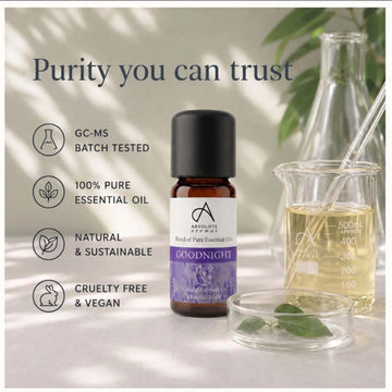 A bottle of Advanced Herbs Goodnight essential oil centered on a styled background with text callouts about purity, batch testing, pure essential oil, natural sustainability, and cruelty-free vegan status. The scene includes a glass beaker with pale yellow liquid, a glass dish with leaves, and soft shadow lighting.
