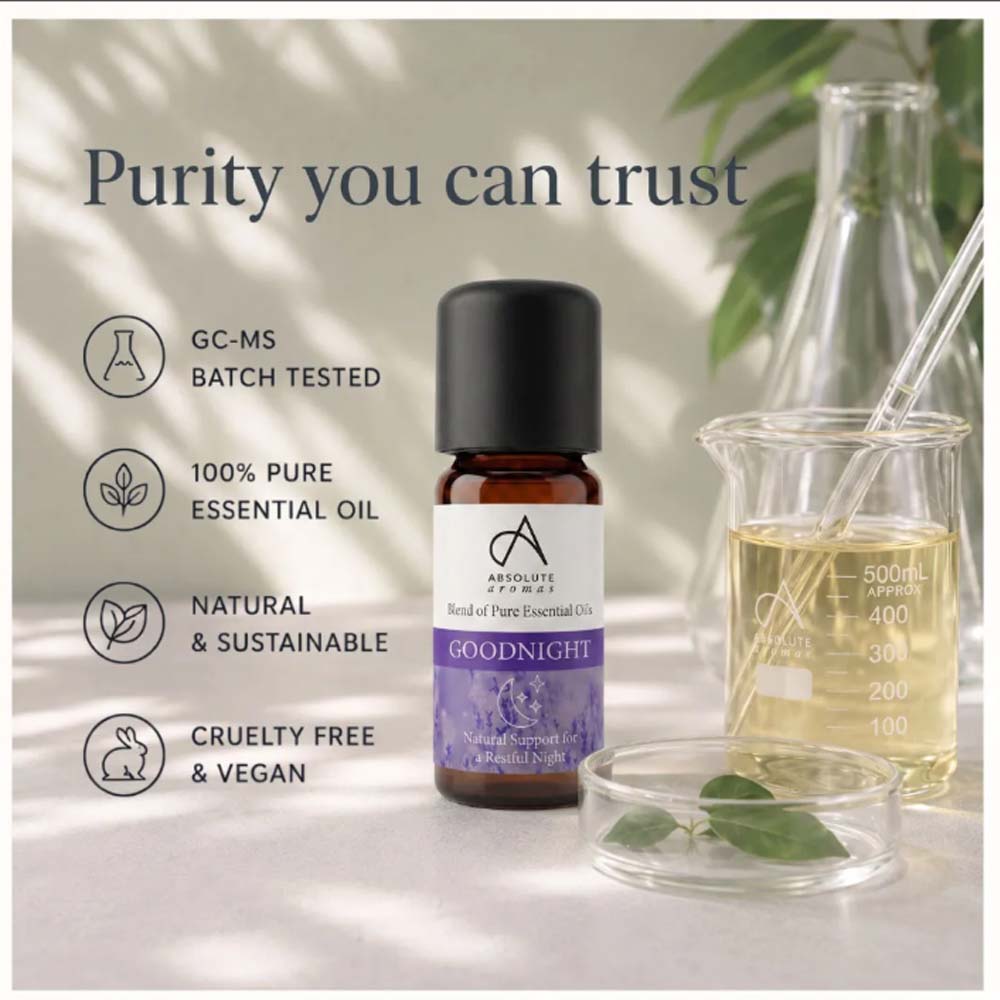 A bottle of Advanced Herbs Goodnight essential oil centered on a styled background with text callouts about purity, batch testing, pure essential oil, natural sustainability, and cruelty-free vegan status. The scene includes a glass beaker with pale yellow liquid, a glass dish with leaves, and soft shadow lighting.