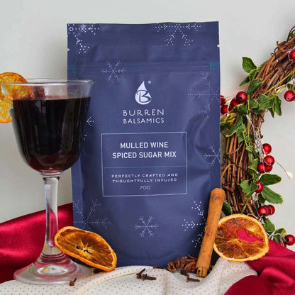 Festive holiday display featuring a pouch of Burren Balsamics Mulled Wine Spiced Sugar Mix alongside a glass of warm mulled wine, dried orange slices, cinnamon sticks, whole cloves, and a Christmas wreath.