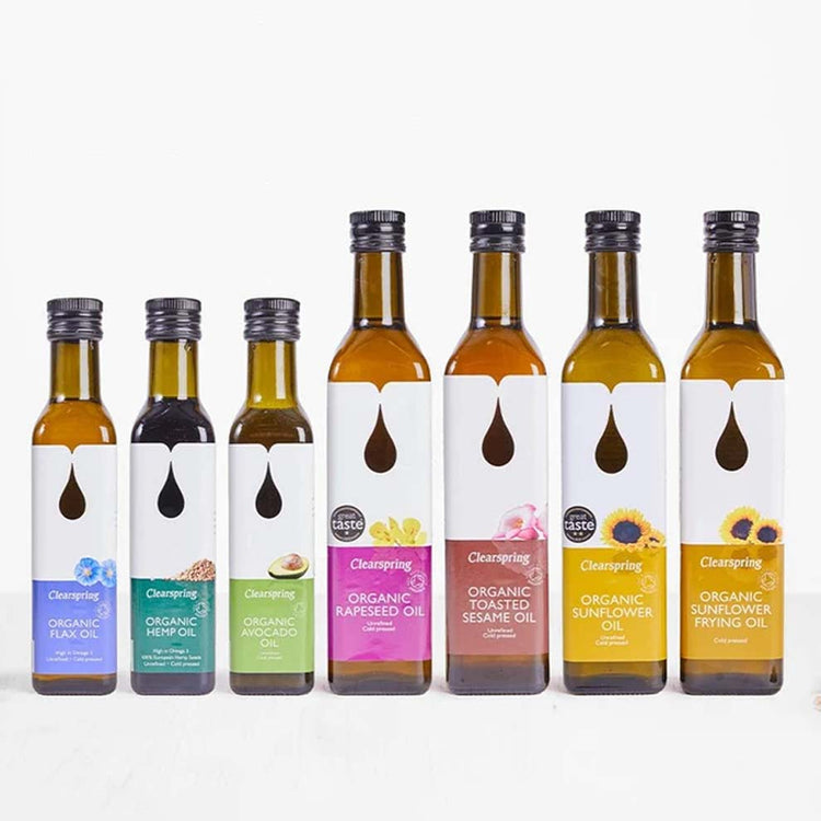 Seven Clearspring organic vegetable and nut butters in glass bottles with white labels and black caps, arranged in a row against a clean white background.