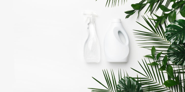 Clear cleaning product bottles on white background with green leaves
