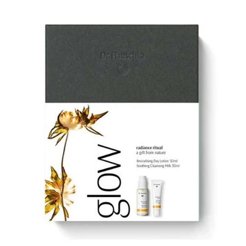 Dr. Hauschka Glow Radiance Ritual set packaging, featuring a dark charcoal gray top section and a white bottom section with gold botanical illustrations and product tubes.