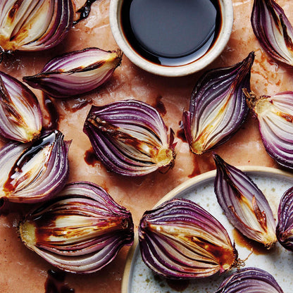 Roasted red onion slices with charred edges, arranged on parchment paper with a small bowl of dark balsamic dressing.