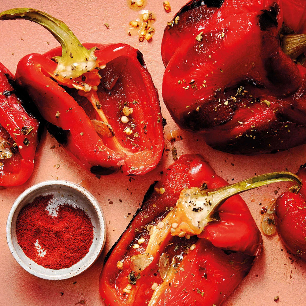 Roasted red peppers with a small bowl of paprika.