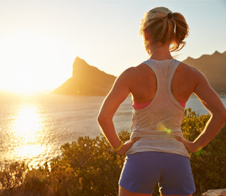 Woman standing by a scenic lakeside at sunset, wearing athletic wear.