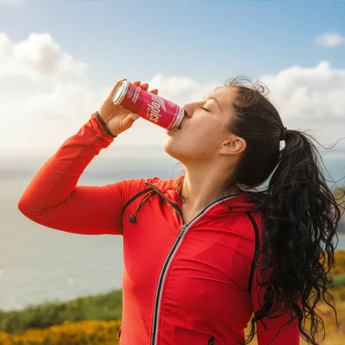 Person in red jacket drinking from a can outdoors
